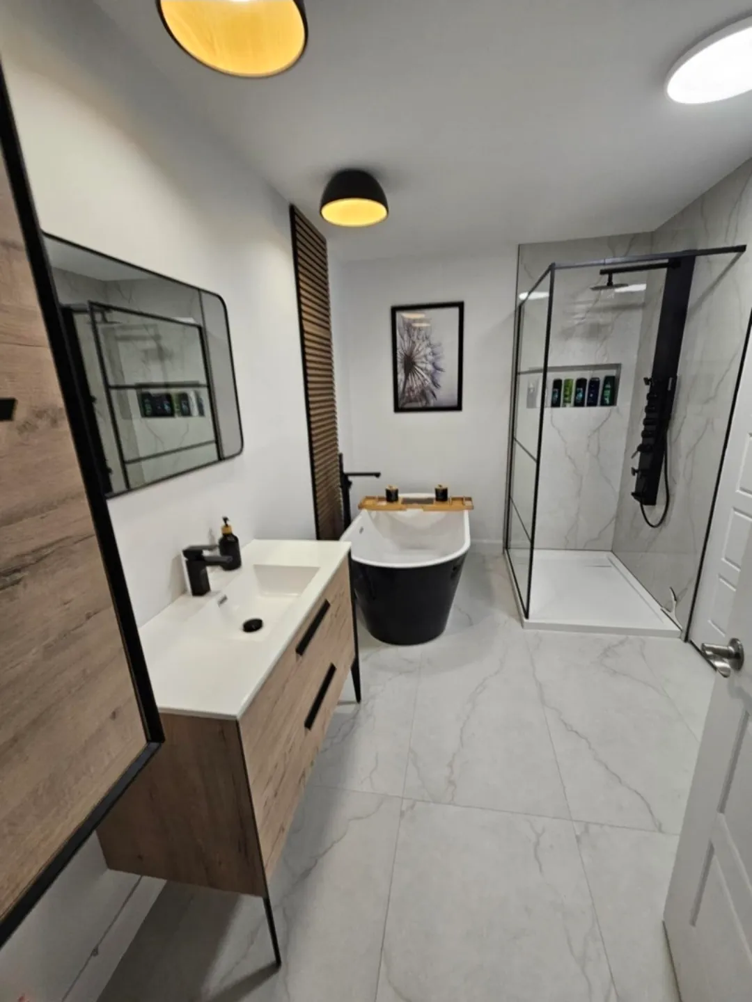 Salle de bain terminée avec robinetterie noire, meuble-lavabo en bois et douche vitrée